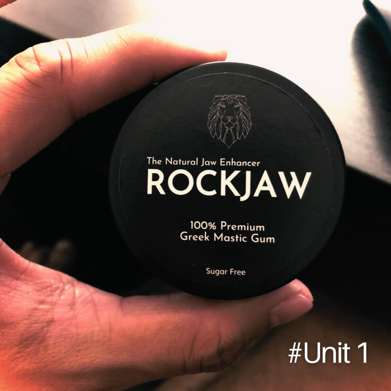 A hand holding the first ROCKJAW tin, labelled The Natural Jaw Enhancer, 100% Premium Greek Mastic Gum, Sugar Free